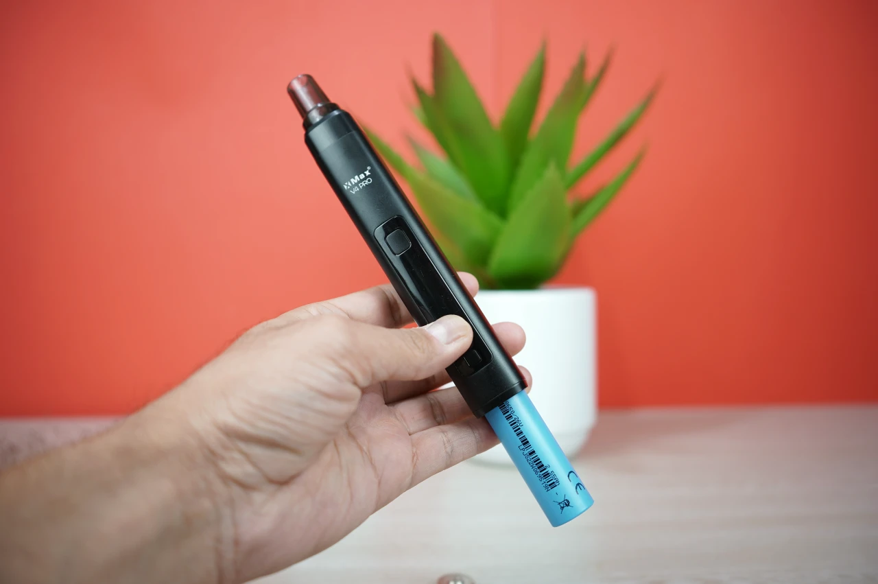 Hand holding black XMAX V4 Pro vaporizer showing blue 18650 replaceable battery removal